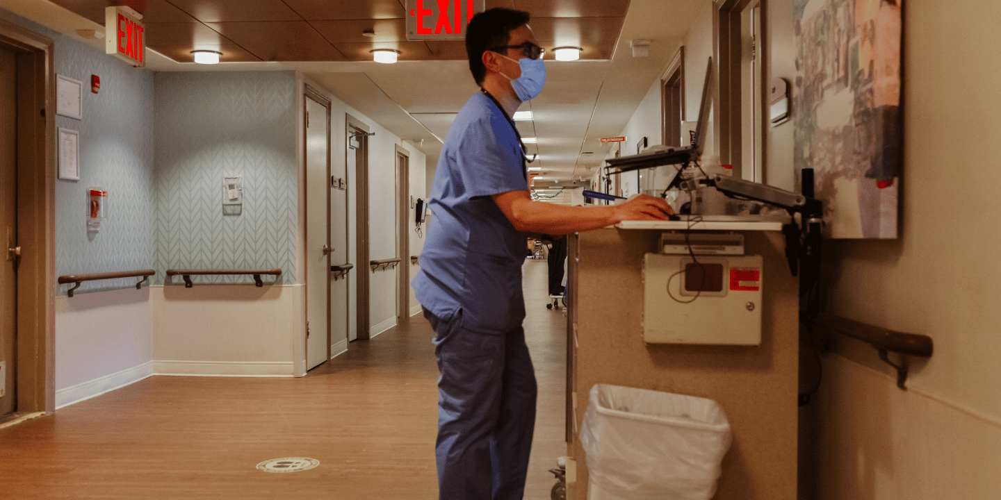 Wound care nurse wearing scrubs in hallway on laptop