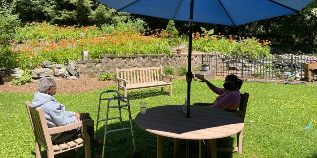 A patient and family member enjoying a visit in the Methodist Home gardens under an umbrella