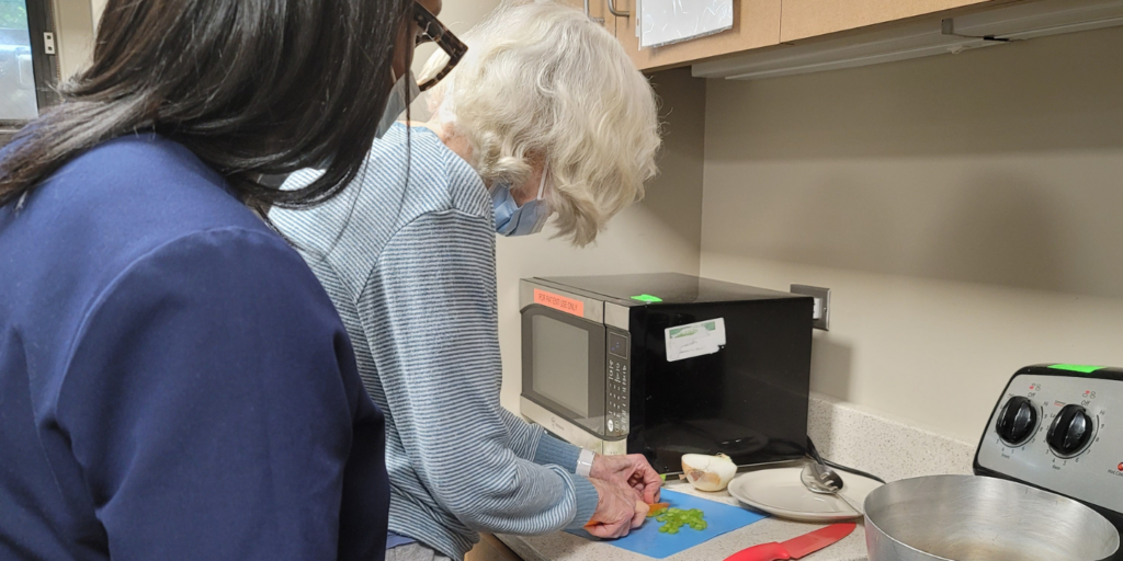 Woman chopping vegetables with therapist supervision during occupational therapy session as part of short term rehab stay.