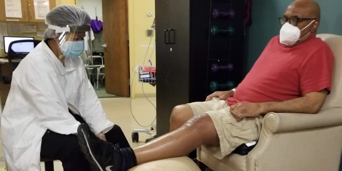 Senior man sitting in chair doing leg exercise after joint replacement as part of therapy session