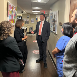 Photo of Councilman Eric Dinowitz standing in hallway of the Methodist Home talking to Administrator and CEO Maria Perez, with other staff members in presence