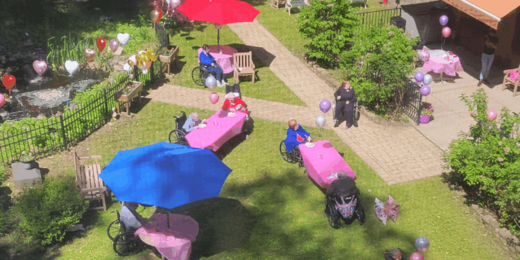 Overhead shot taken of the Methodist Home gardens set up for a fun outdoor party, with colorful tablecloths, umbrellas, and balloons and residents enjoying the sunny day