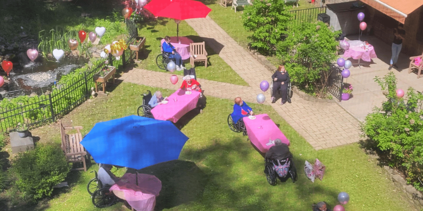 Overhead shot taken of the Methodist Home gardens set up for a fun outdoor party, with colorful tablecloths, umbrellas, and balloons and residents enjoying the sunny day