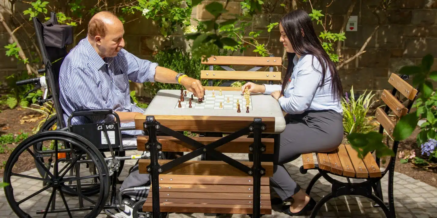 Senior man enjoying a game of chess with a female employee outside in the beautiful garden area at the Methodist Home during his short term rehabilitation stay. Positive Mindset